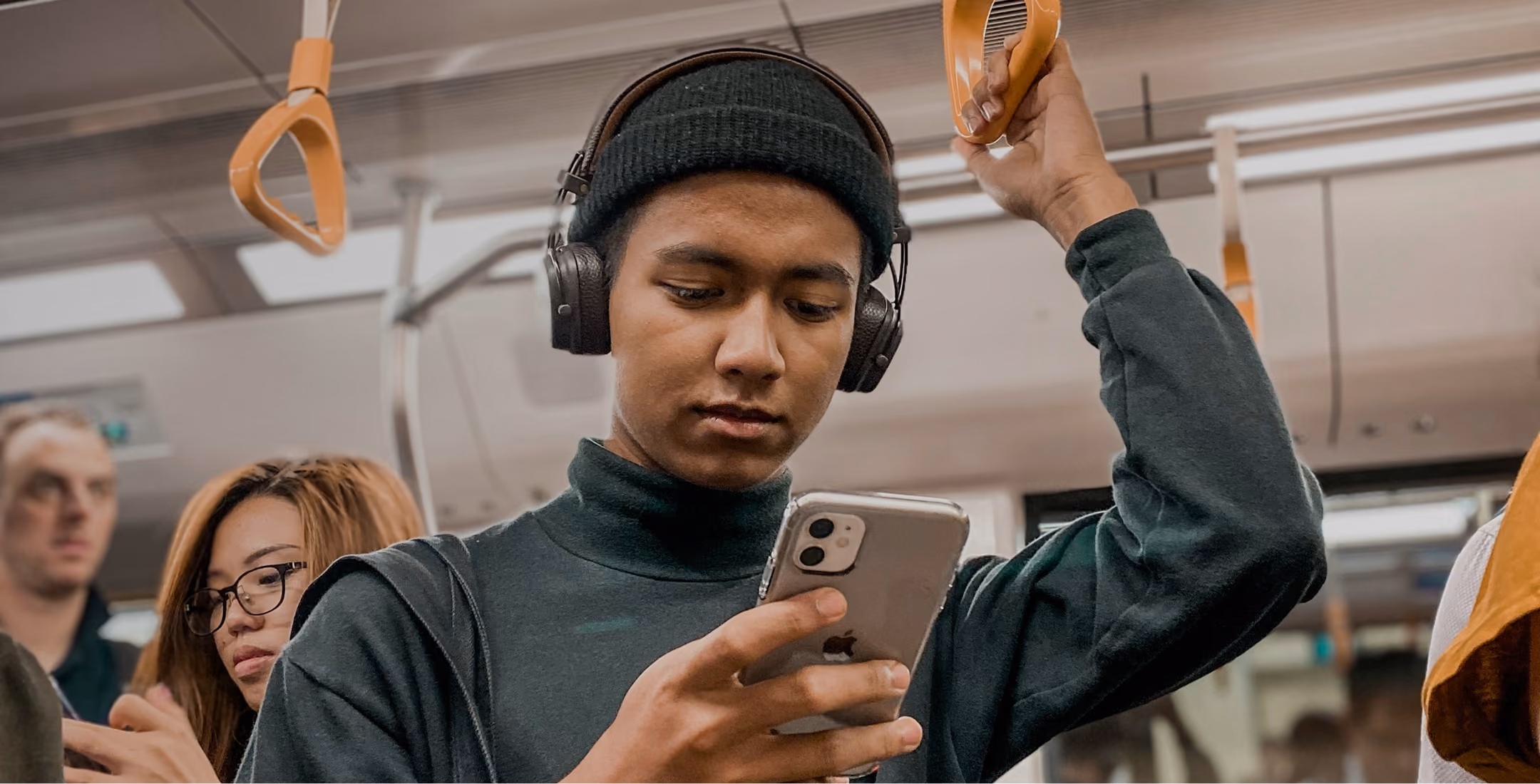 man with headphones looking at phone on subway