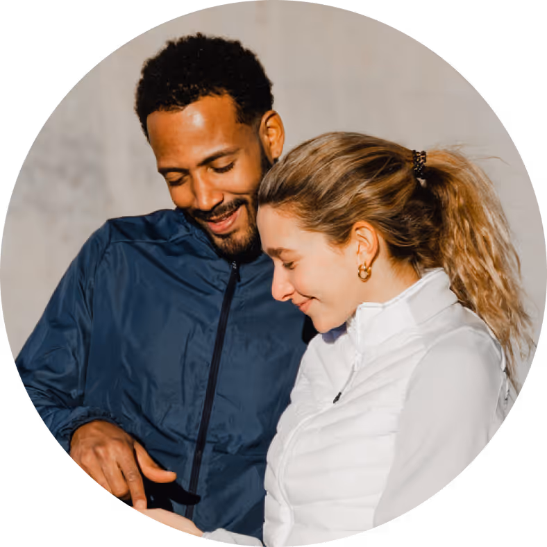 Smiling man in a blue jacket and woman in a white jacket looking down together.