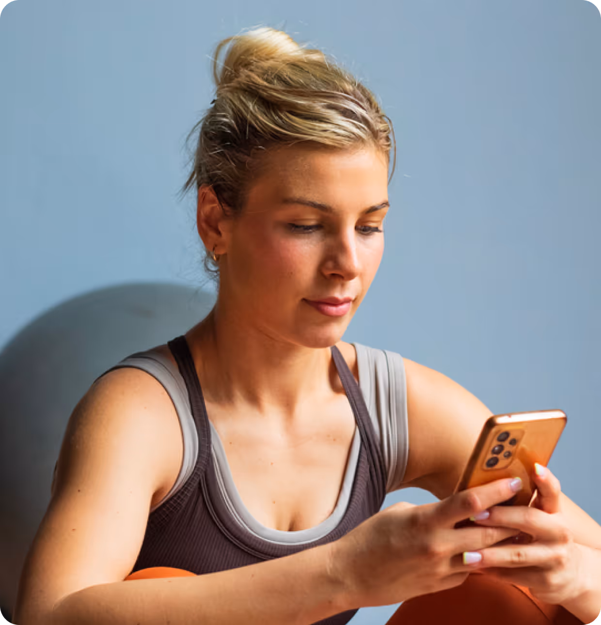 Young woman in workout attire looking at her smartphone with a gym ball in the background.