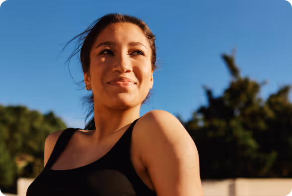 Smiling woman outdoors in a black tank top with trees and blue sky in the background.