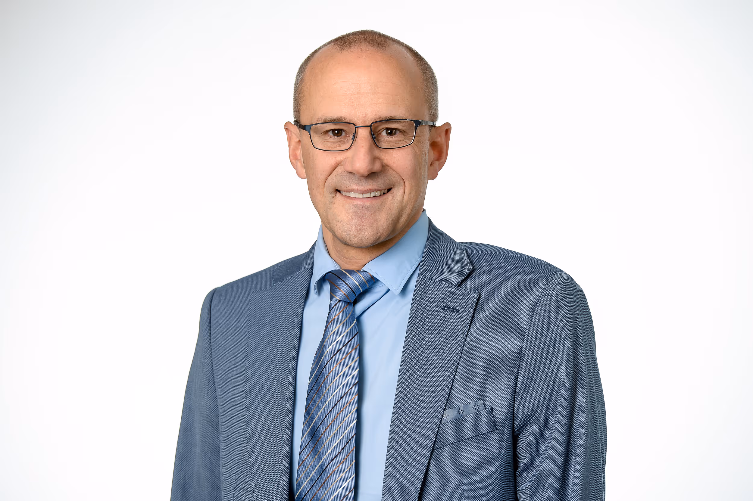 Porträt eines lächelnden Mannes mittleren Alters mit Brille in einem blauen Anzug, Hemd und gestreifter Krawatte vor weißem Hintergrund.