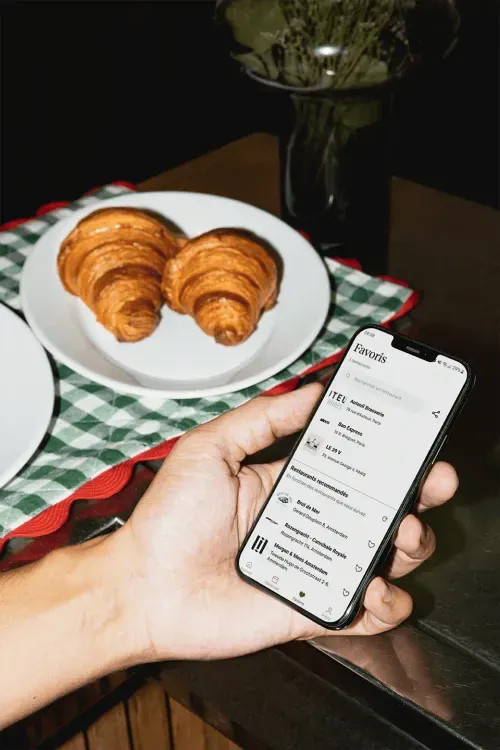 A close-up of a hand holding a smartphone displaying a list of favorite restaurants in French Zenchef app.