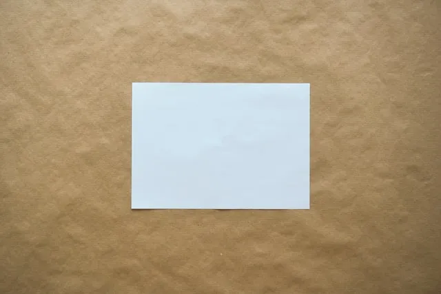 A single blank white sheet of paper centered on a textured brown kraft paper background