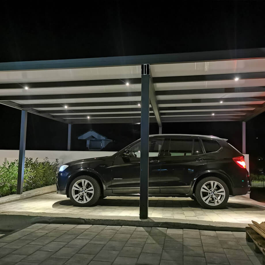 Veranda moderna, inchisa cu sticla, cu o masa de luat masa si scaune, construita pe o baza de piatra, adiacenta unei case galbene.