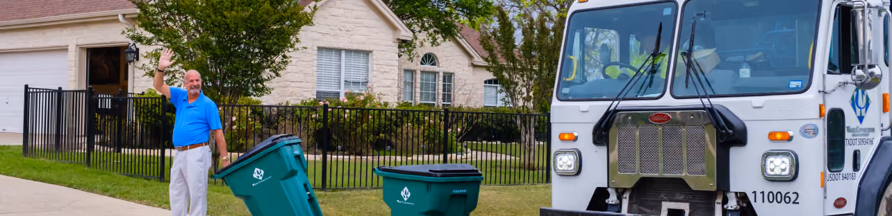 Man waving to a collection truck from his curb with a recycling bin