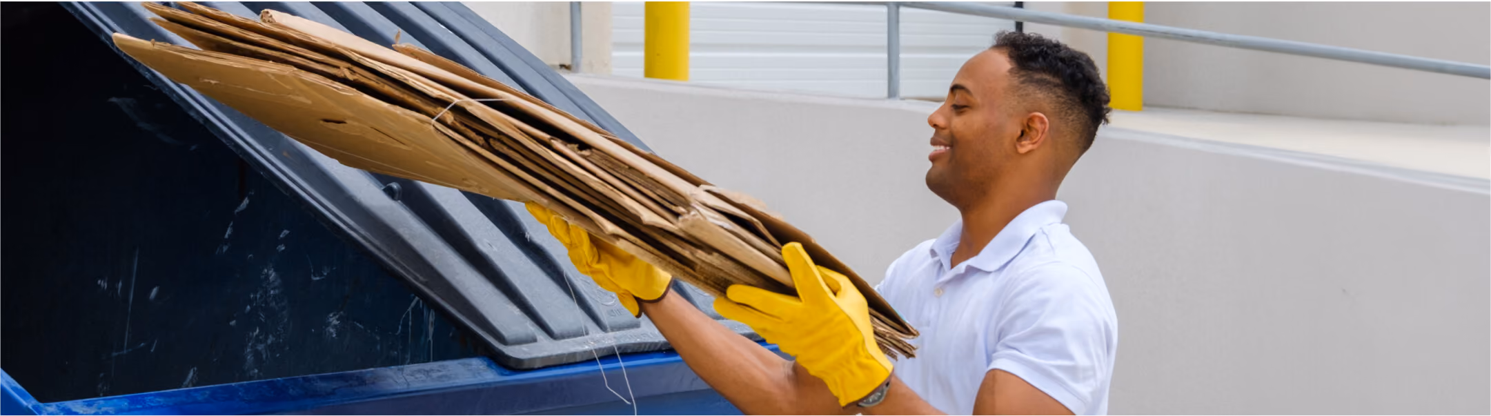 Worker loading flattened cardboard into a commercial recycling bin