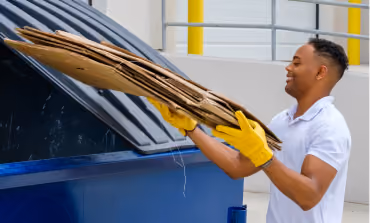 Man in work gloves loading flattened cardboard into a blue container
