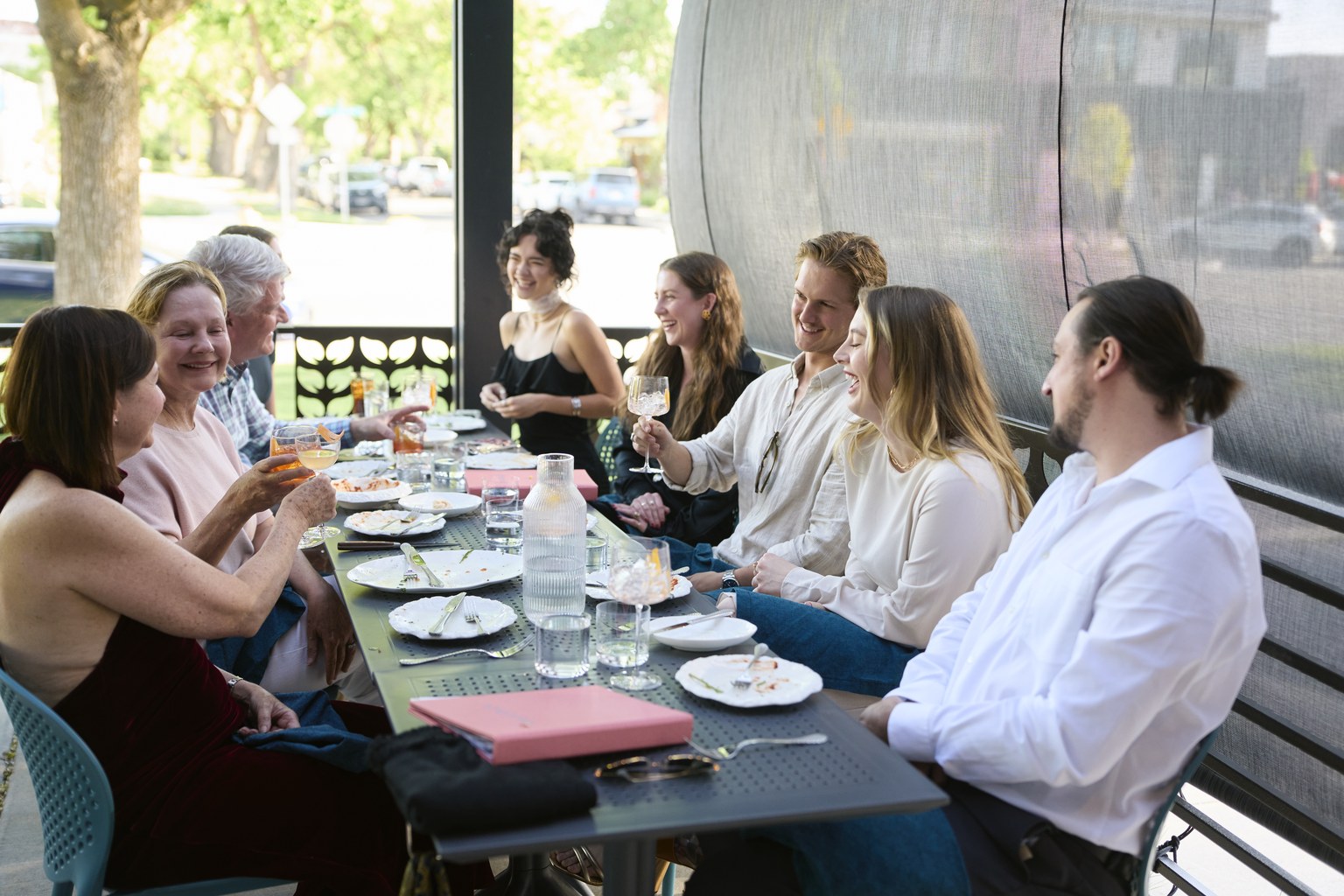 A long table of friends and family on the patio at 'mina, plates cleared and glasses raised at the end of a meal.