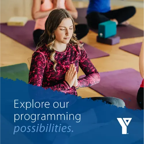 Young women in yoga class meditating with overlay with YMCA logo that reads “explore our programming possibilities”.