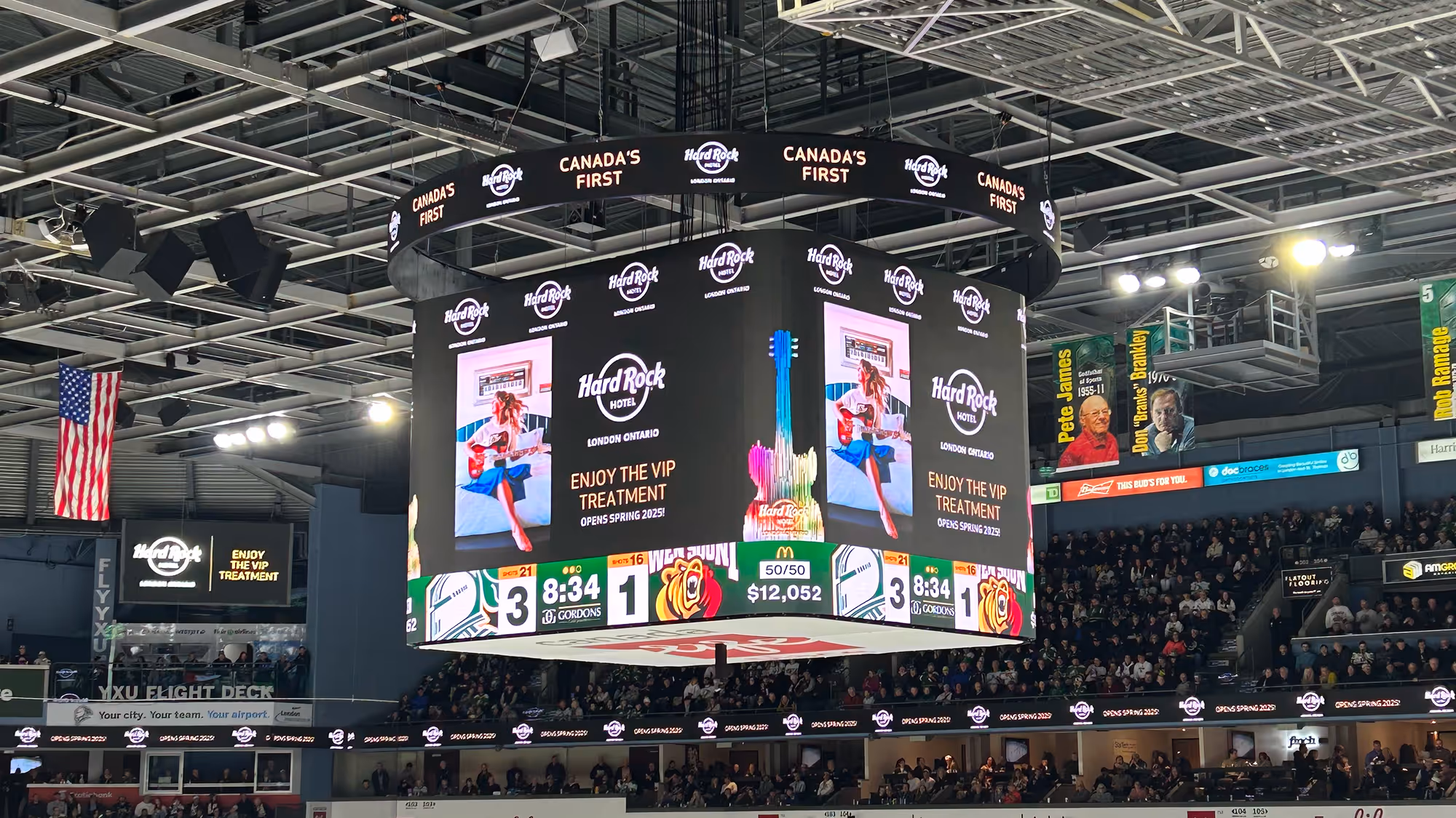 Large indoor arena scoreboard displaying Hard Rock Hotel London Ontario ads and a hockey game score with a crowd in the stands.