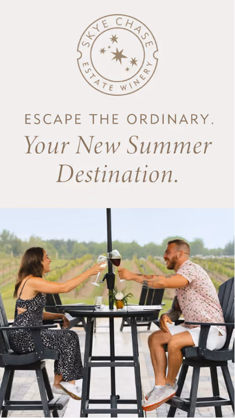 Digital Ad: Skye Chase Estate Winery logo above text reading 'Escape the Ordinary. Your New Summer Destination.' Below, a woman and man sitting outdoors at a table with wine glasses raised in a toast, with vineyard rows visible in the background.