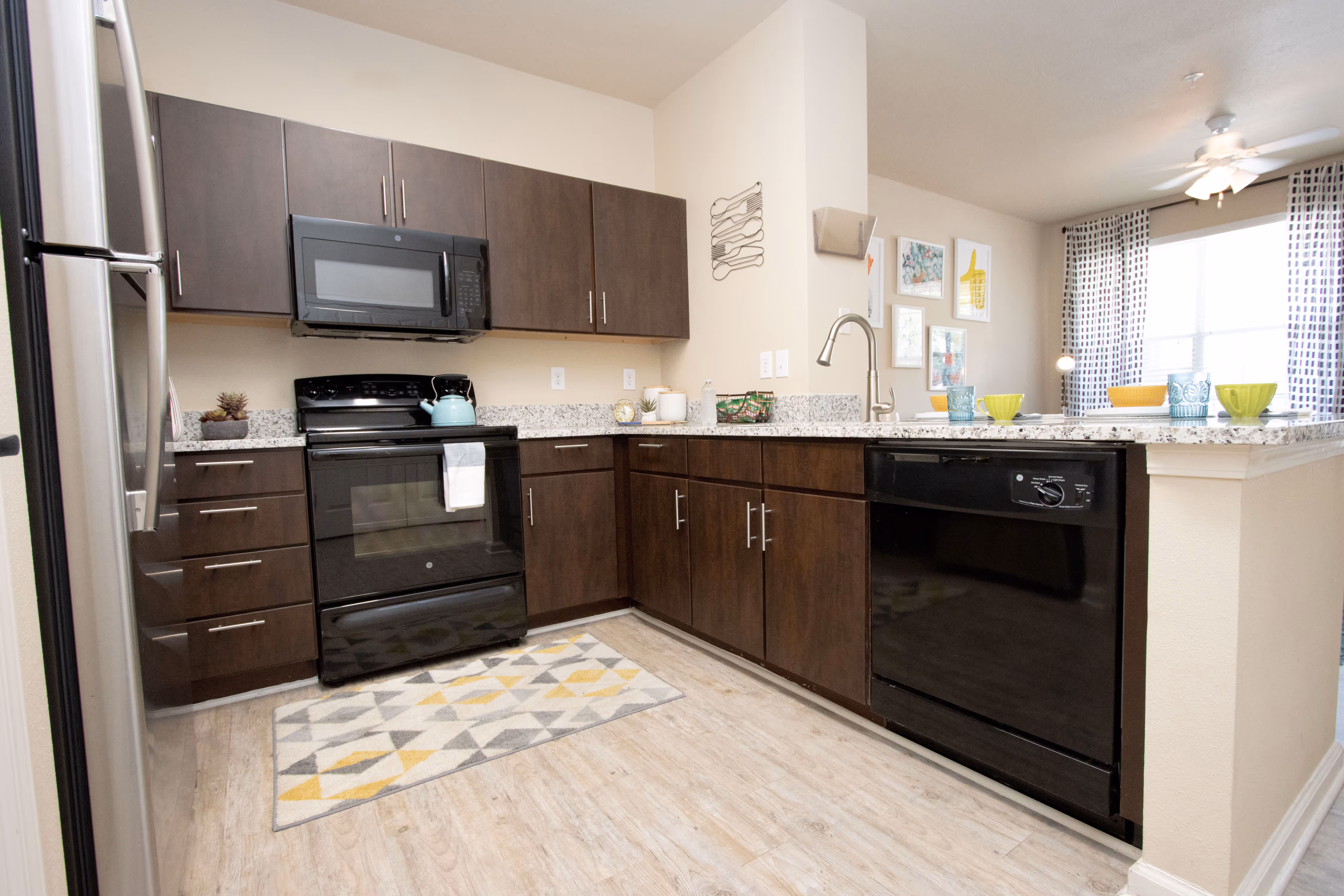 Modern apartment kitchen with dark wood cabinets, black appliances, and a bar area overlooking the living space at Rev Oxford in Oxford, MS.