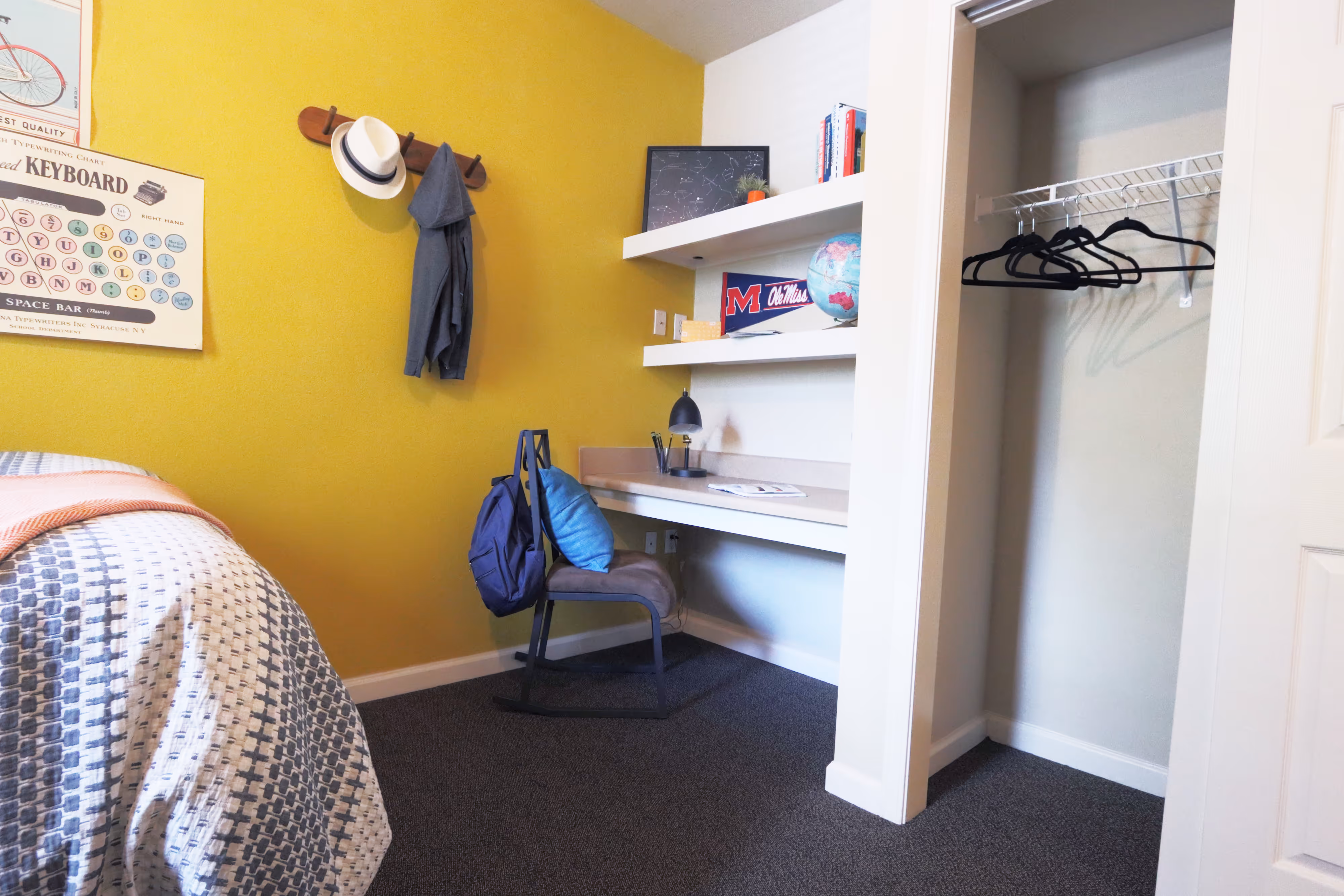 Student apartment bedroom with a yellow accent wall, built-in desk, and closet space, ideal for studying at Rev Oxford in Oxford, MS.