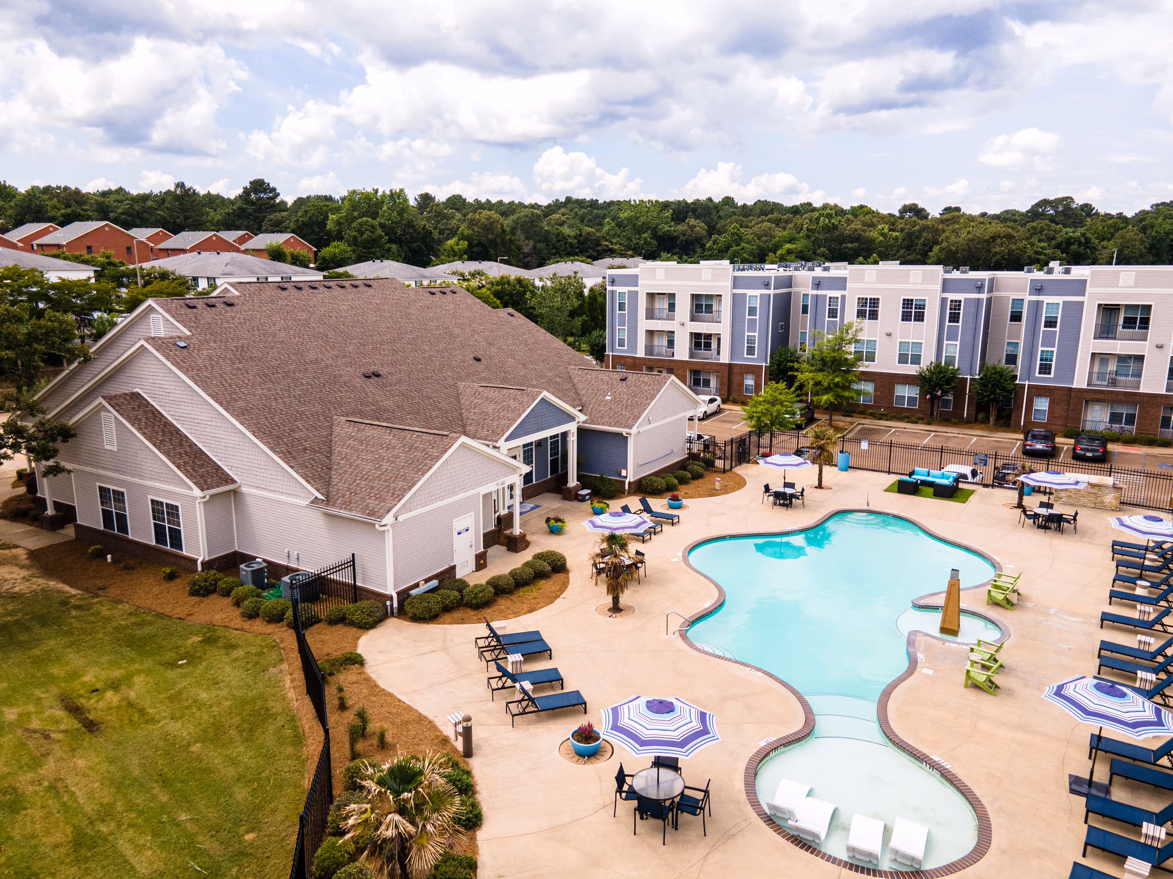 Aerial view of the student apartment community, showcasing the clubhouse, unique-shaped swimming pool, and modern gray apartment buildings at Rev Oxford in Oxford, MS.
