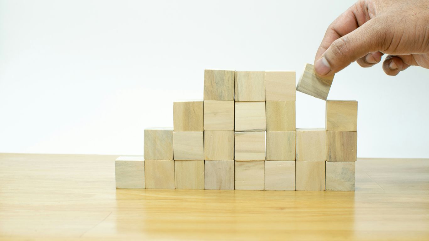 A person placing a block into a pile of wooden blocks