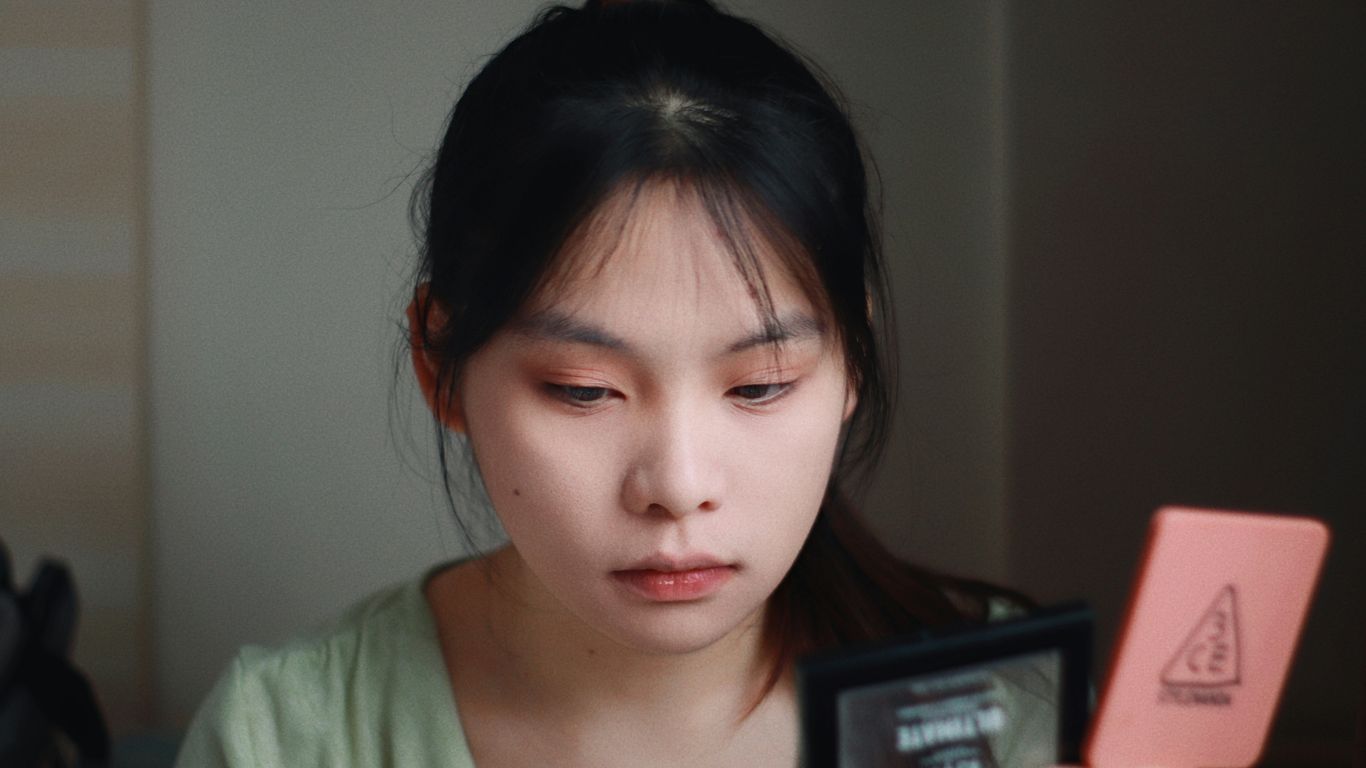 Woman applies makeup, looking in a compact mirror.