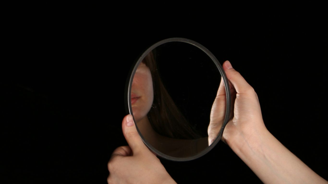 A person holds a mirror, reflecting their face.