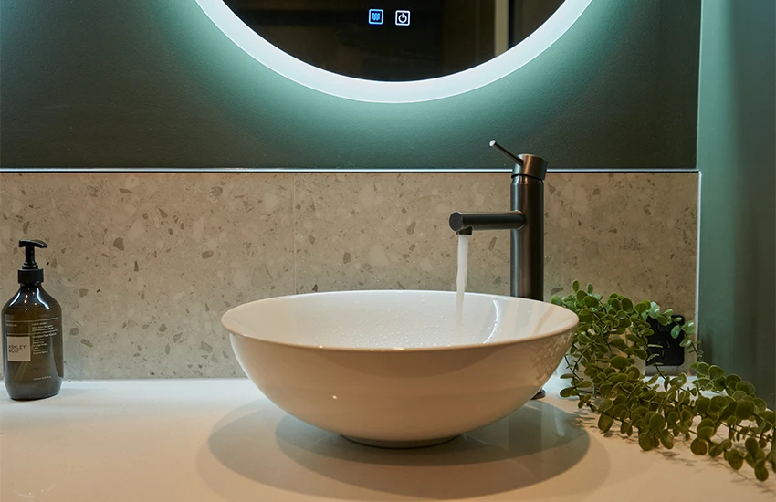 A white freestanding bathroom basin with gunmetal mixer. The tap is turned on letting water flow into basin.