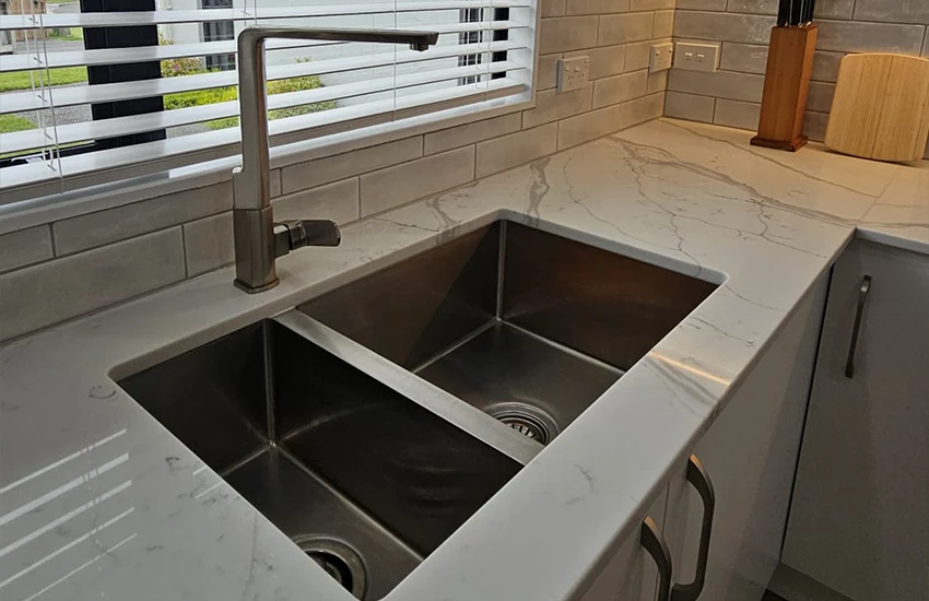 A stainless steel sink with stainless steel kitchen mixer installed into stone benchtop in modern kitchen