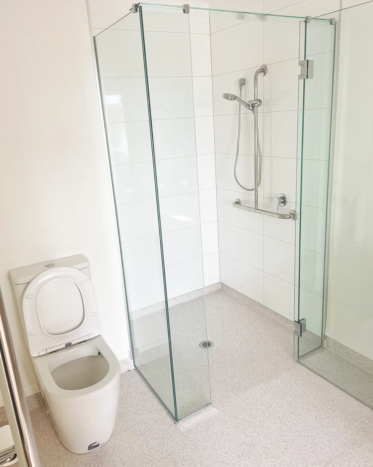 Level-entry glass shower with slip-resistant flooring, a grab rail and a slide-rail handshower
