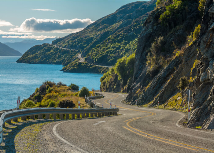 Carretera costera sinuosa junto a un lago de montaña bajo cielo parcialmente nublado