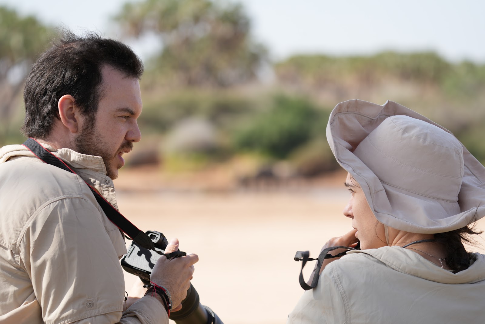Two safari travelers reviewing camera shots together on the sun-baked Kenyan savanna