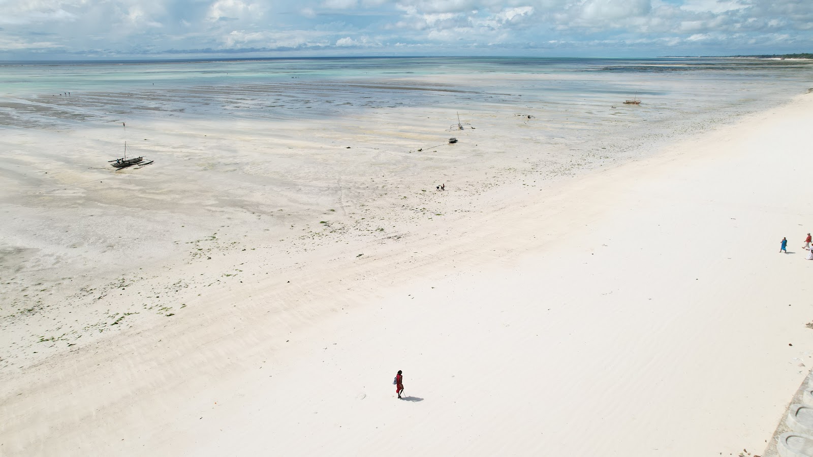 Aerial view of a white sand beach at low tide with a lone figure in red walking
