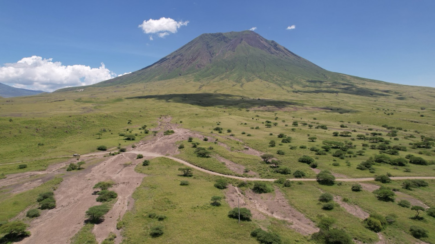 Vista aèria d'una gran muntanya volcànica envoltada de plana verda amb acacies i pistes de terra