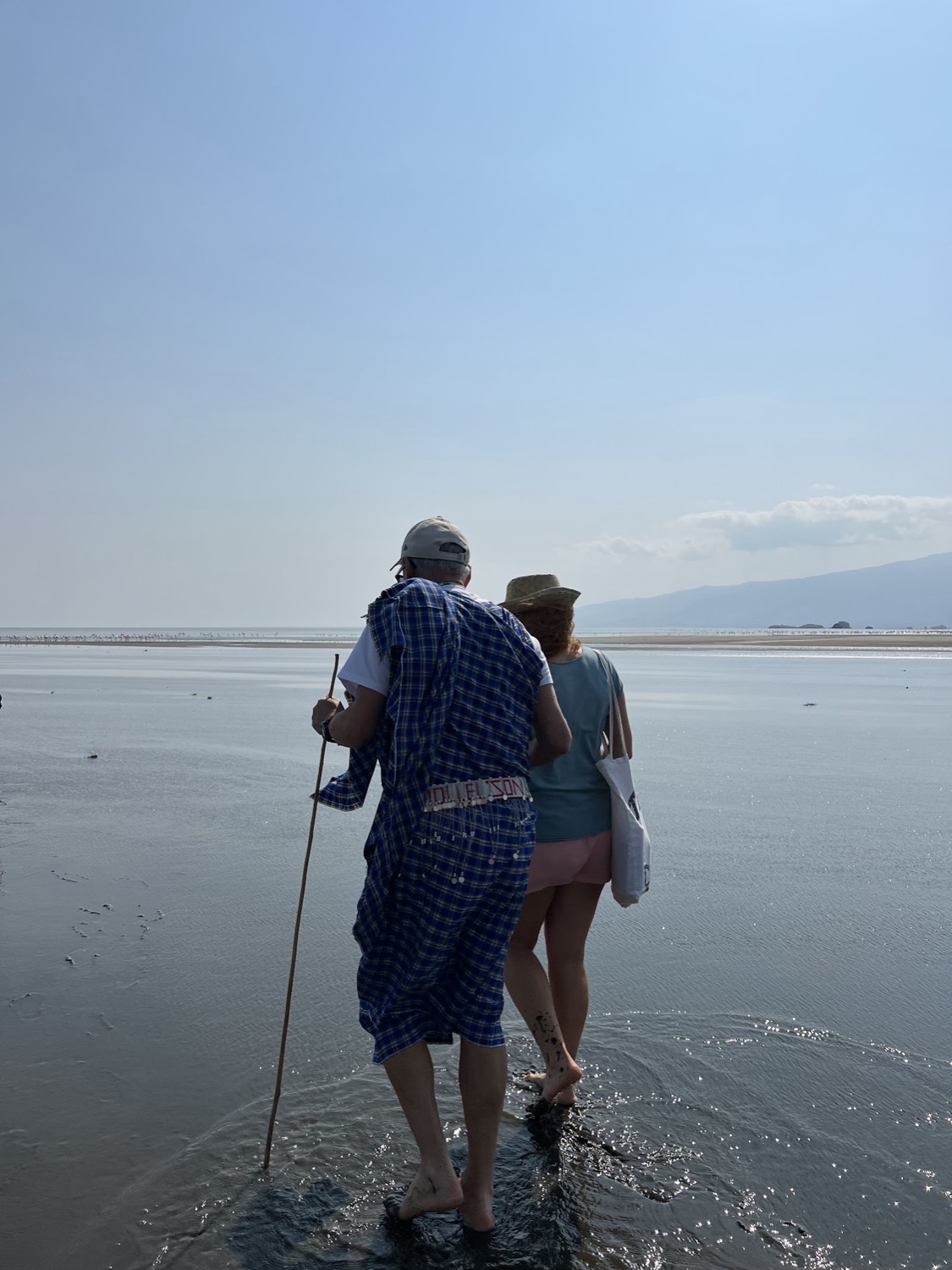 Dos turistas caminan descalzos por aguas poco profundas hacia una bandada de flamencos lejanos