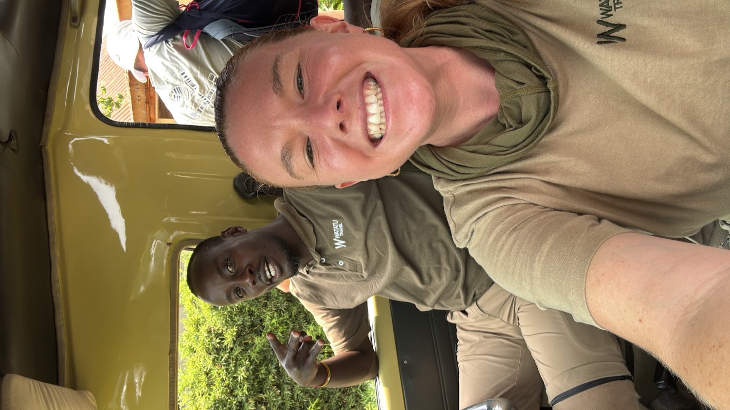 Turista sonriente en vehículo safari junto a guía con uniforme Watatu Tours