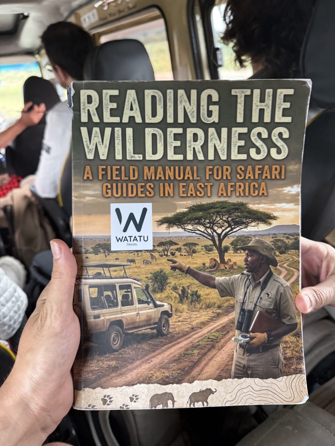 Mà sostenint el manual 'Reading the Wilderness' per a guies de safari a l'interior d'un vehicle