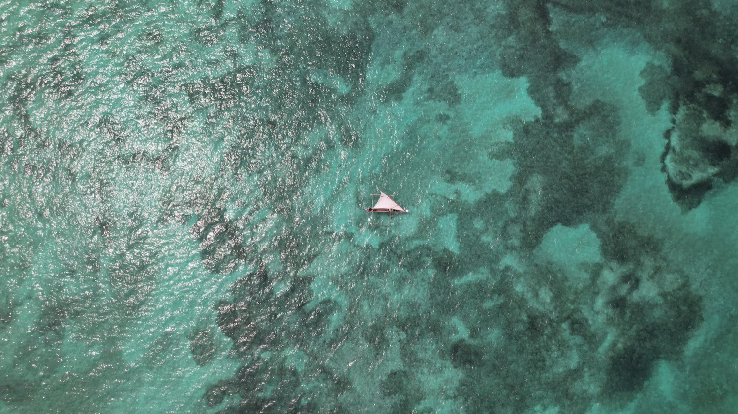 Vista aèria d'una petita embarcació de vela tradicional sobre aigües turqueses amb esculls de coral visibles