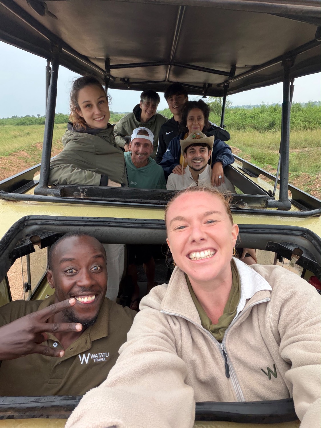 Smiling group of tourists and guides taking a selfie aboard an open-top safari jeep on overcast day