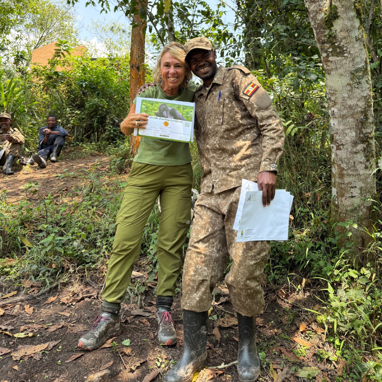 Turista y guarda forestal posan sonriendo con un certificado de seguimiento de gorilas en el bosque