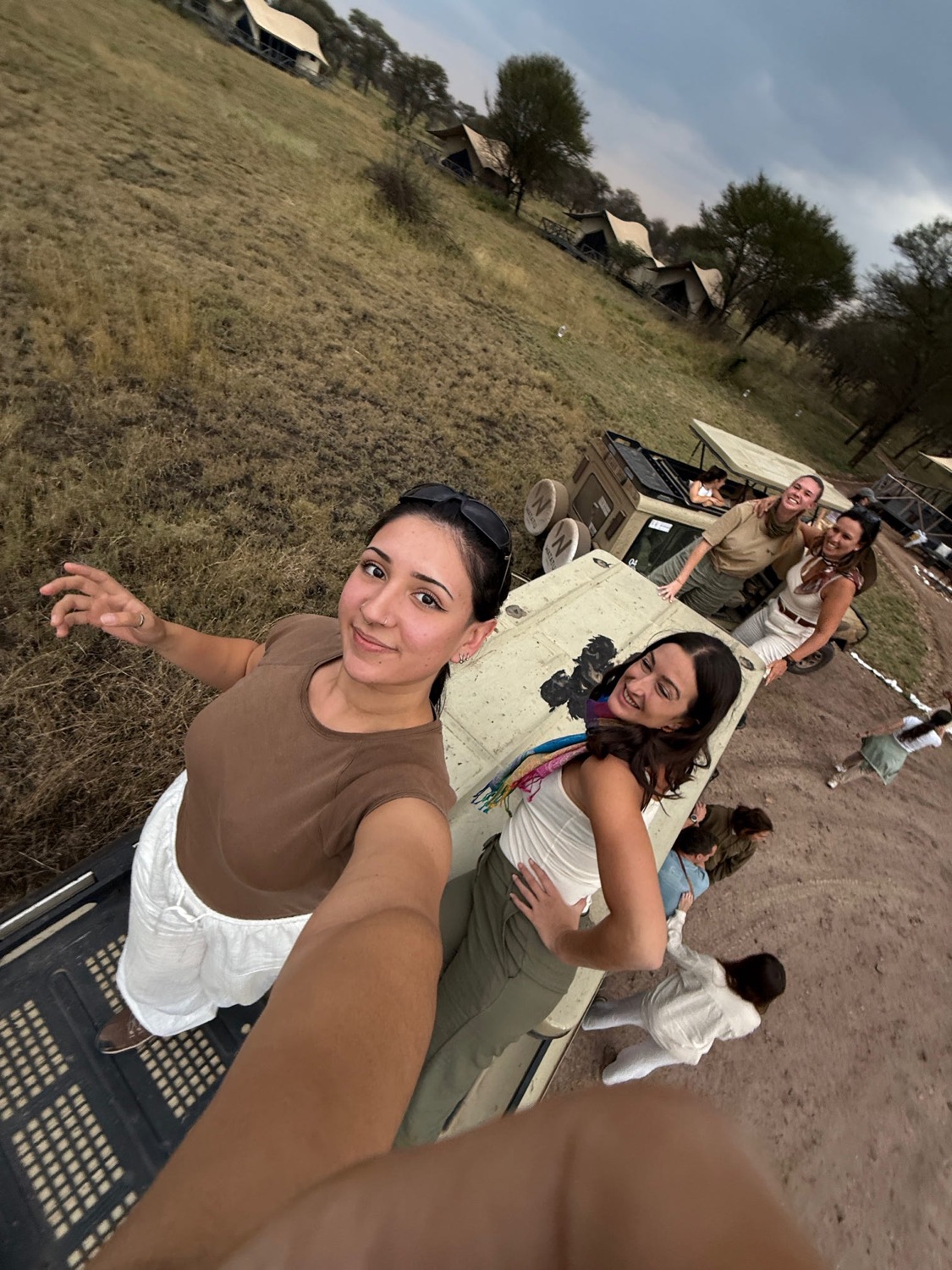 Grupo de mujeres sonrientes junto a un vehículo safari con tiendas de campaña al fondo