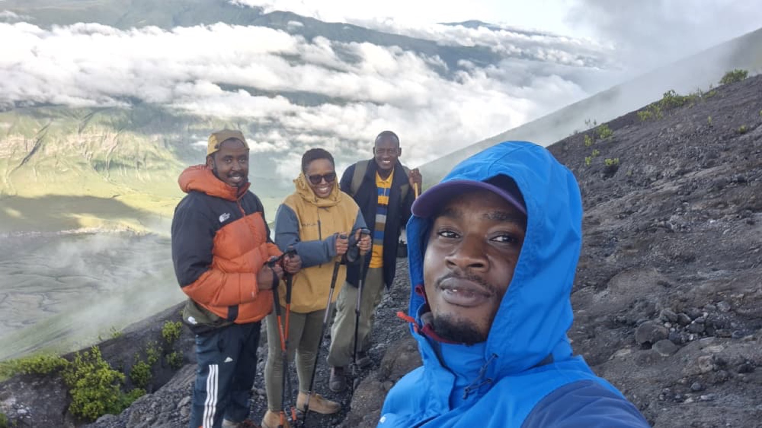 Cuatro excursionistas sonrientes posan en una empinada ladera volcánica sobre las nubes