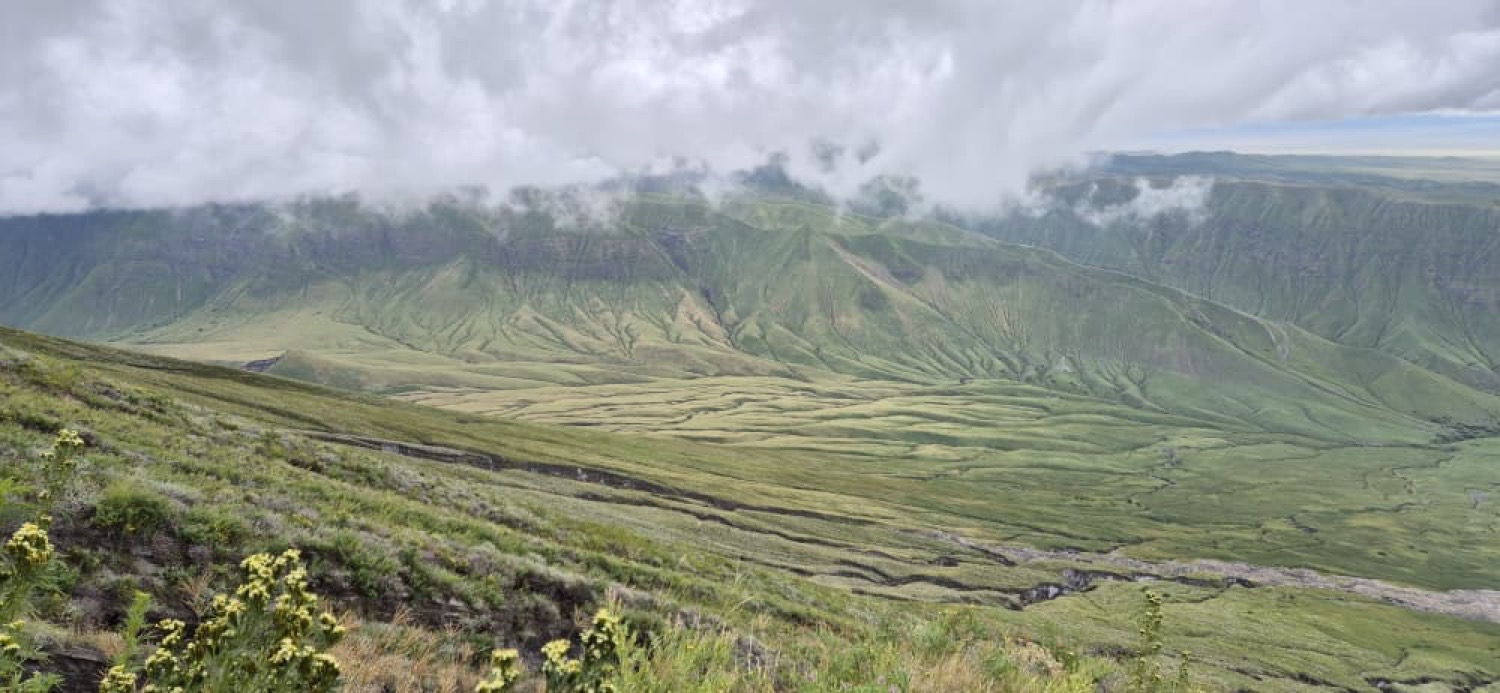 Amplio valle volcánico verde con paredes escarpadas y nubes bajas al fondo