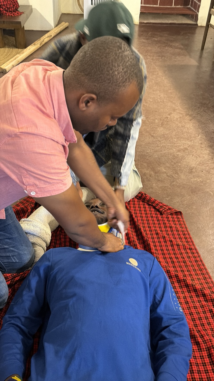 Man practises first aid on a person lying on a red checked blanket indoors