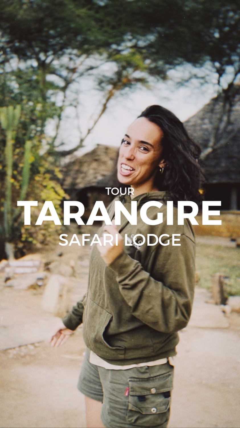 Smiling woman in safari clothes posing in front of a thatched-roof lodge surrounded by trees