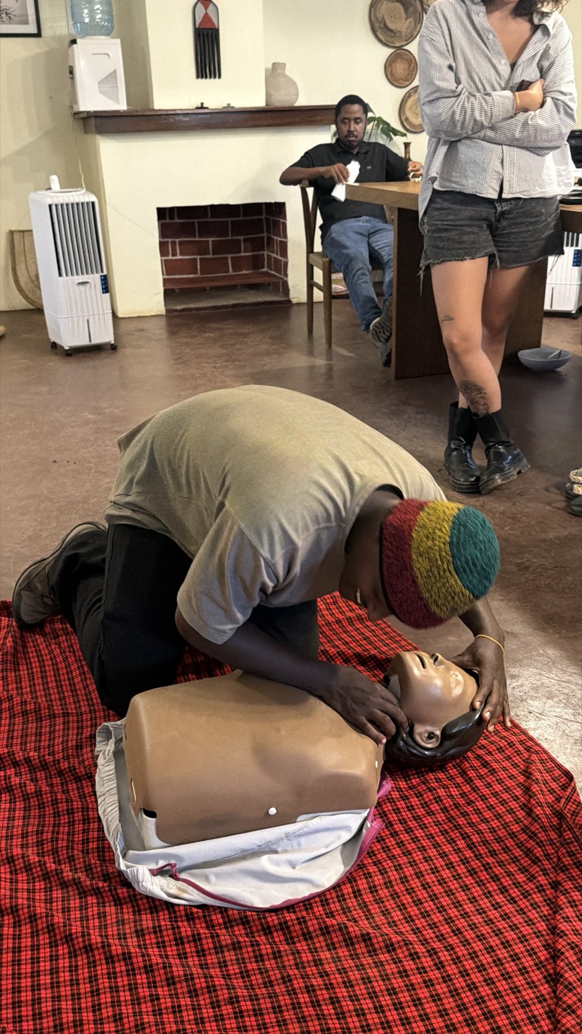 Person kneeling over a CPR training mannequin on a red blanket indoors