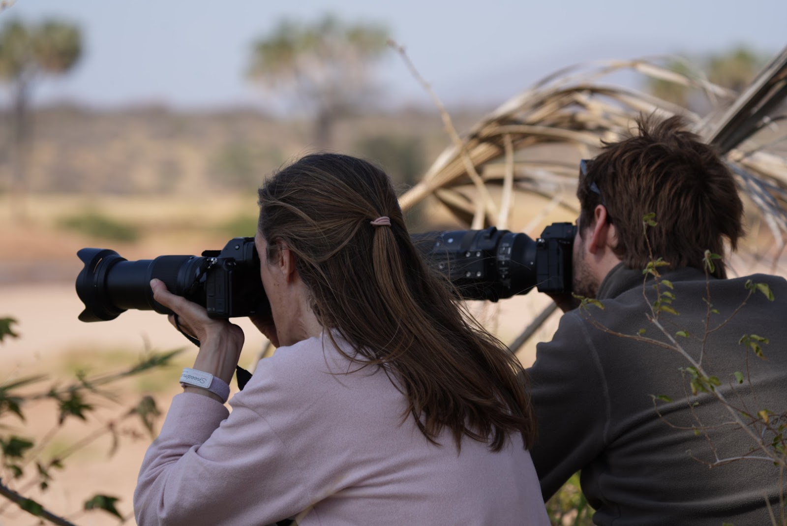 Two photographers aim telephoto lenses across the dry Kenyan savanna on safari