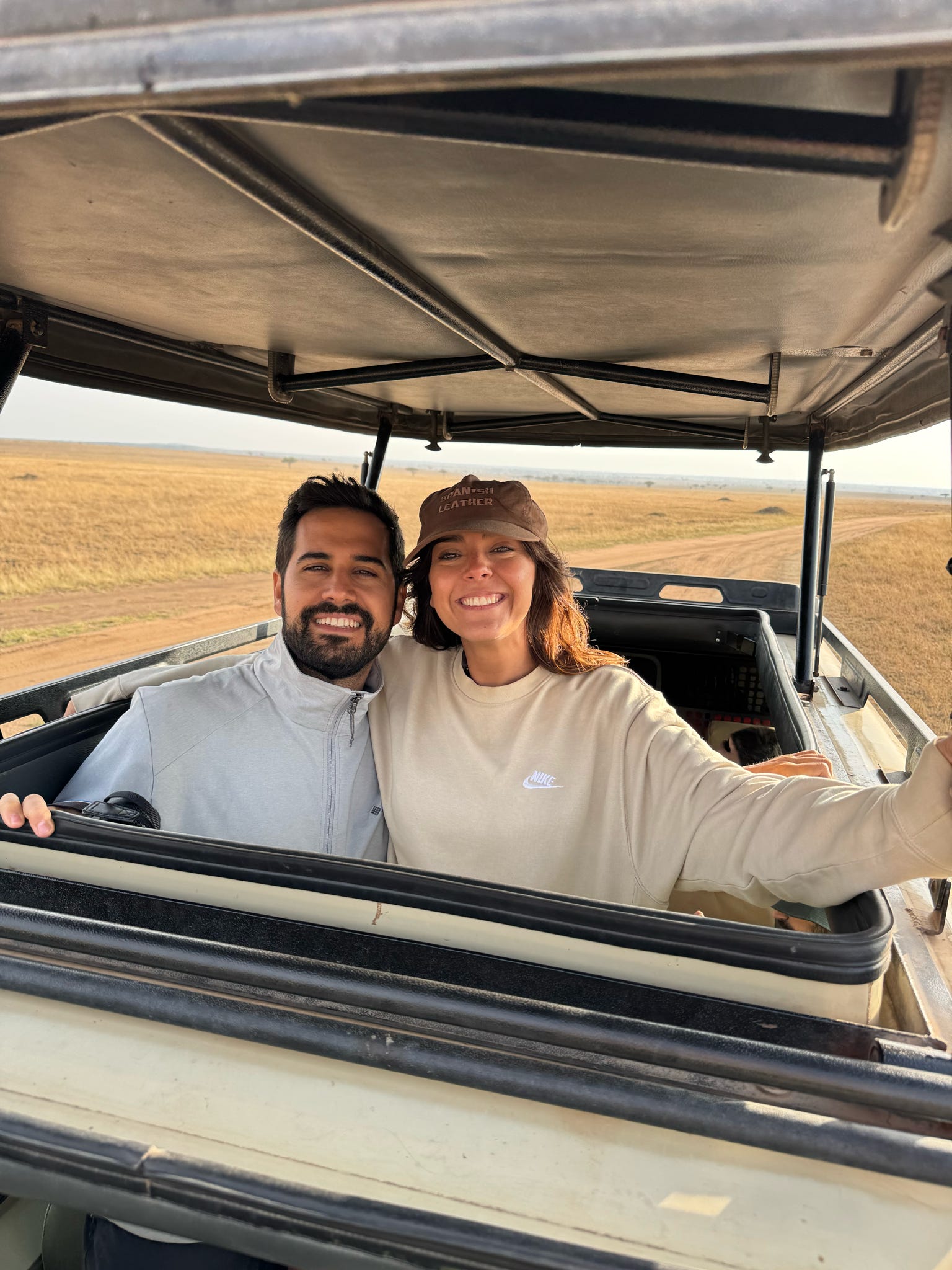 Pareja sonriente asomada por el techo de un vehículo de safari en la sabana tanzana