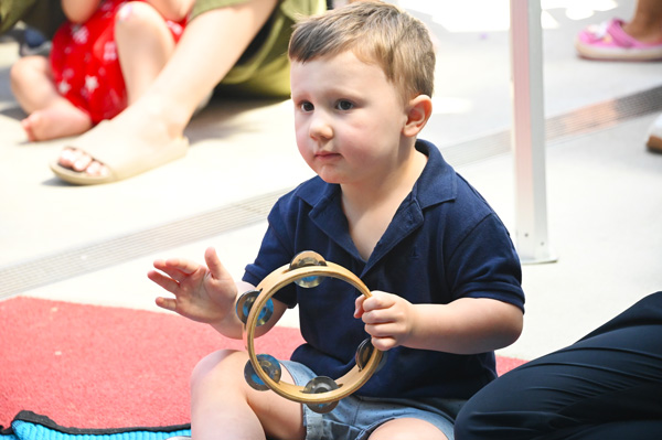 A child in kindy playing the tambourine for music at Little Saints Childcare, Bull Creek WA