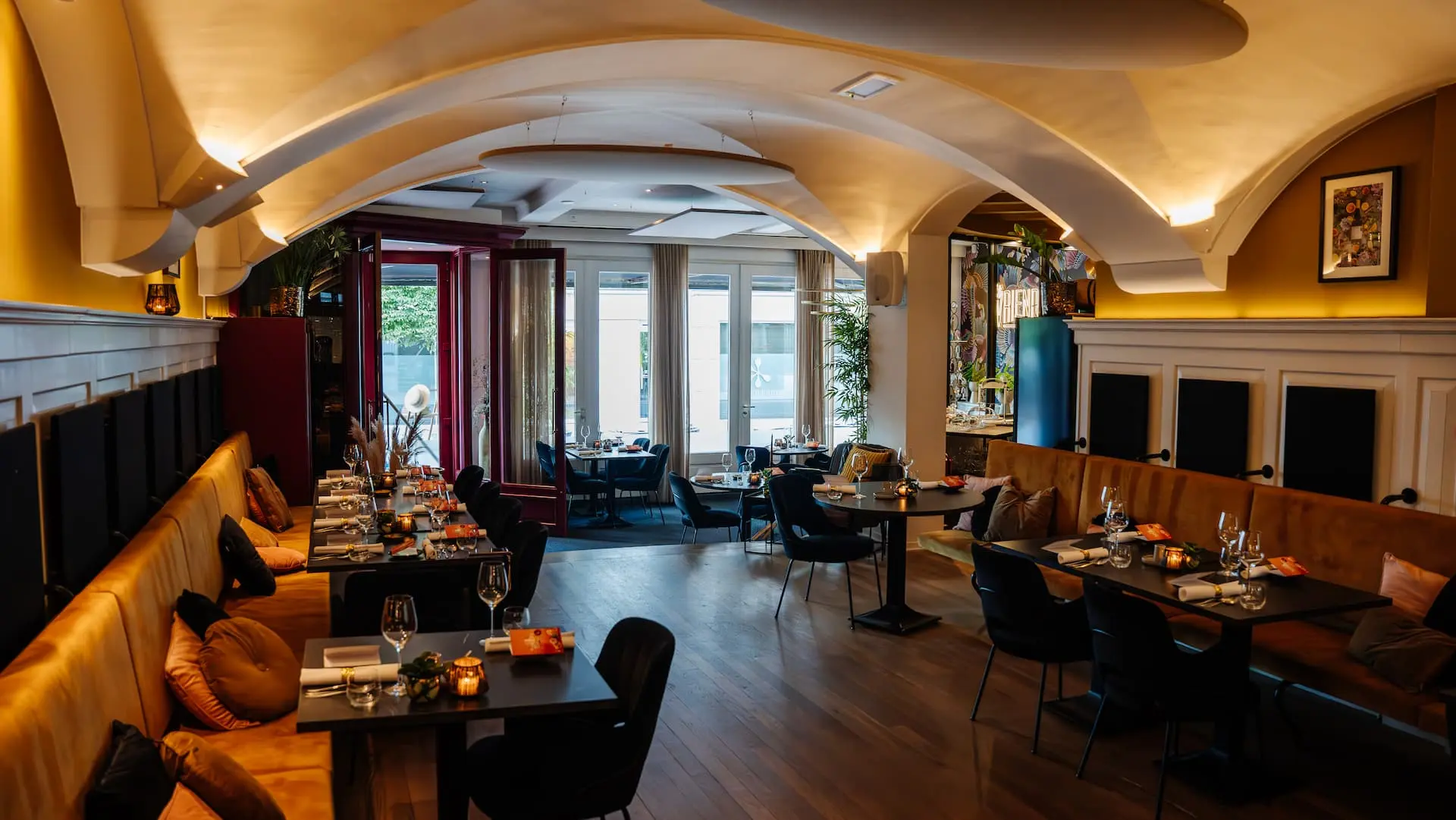A stylish, warmly lit restaurant with arched ceilings, plush seating, and elegantly set tables.