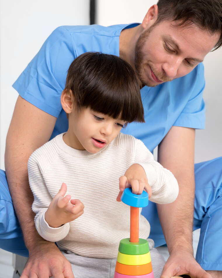A therapist and a child playing with a colorful stacking toy during an in-home ABA session