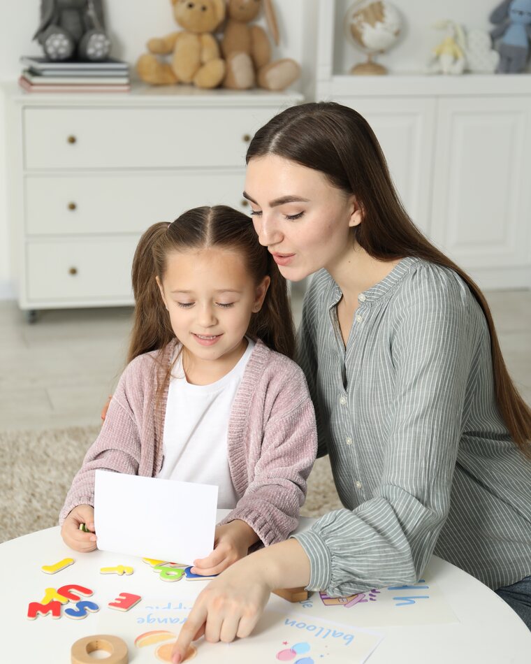 A speech therapist working on letters with a young girl at home