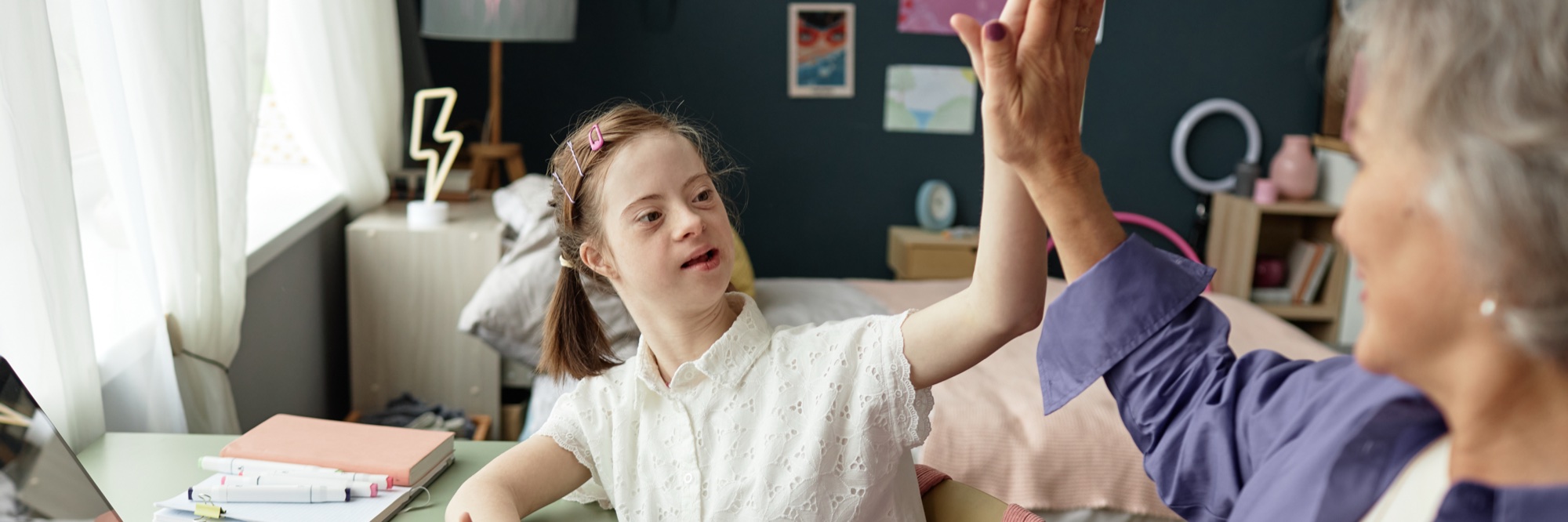 A smiling young girl high-fiving her in-home therapist during a session