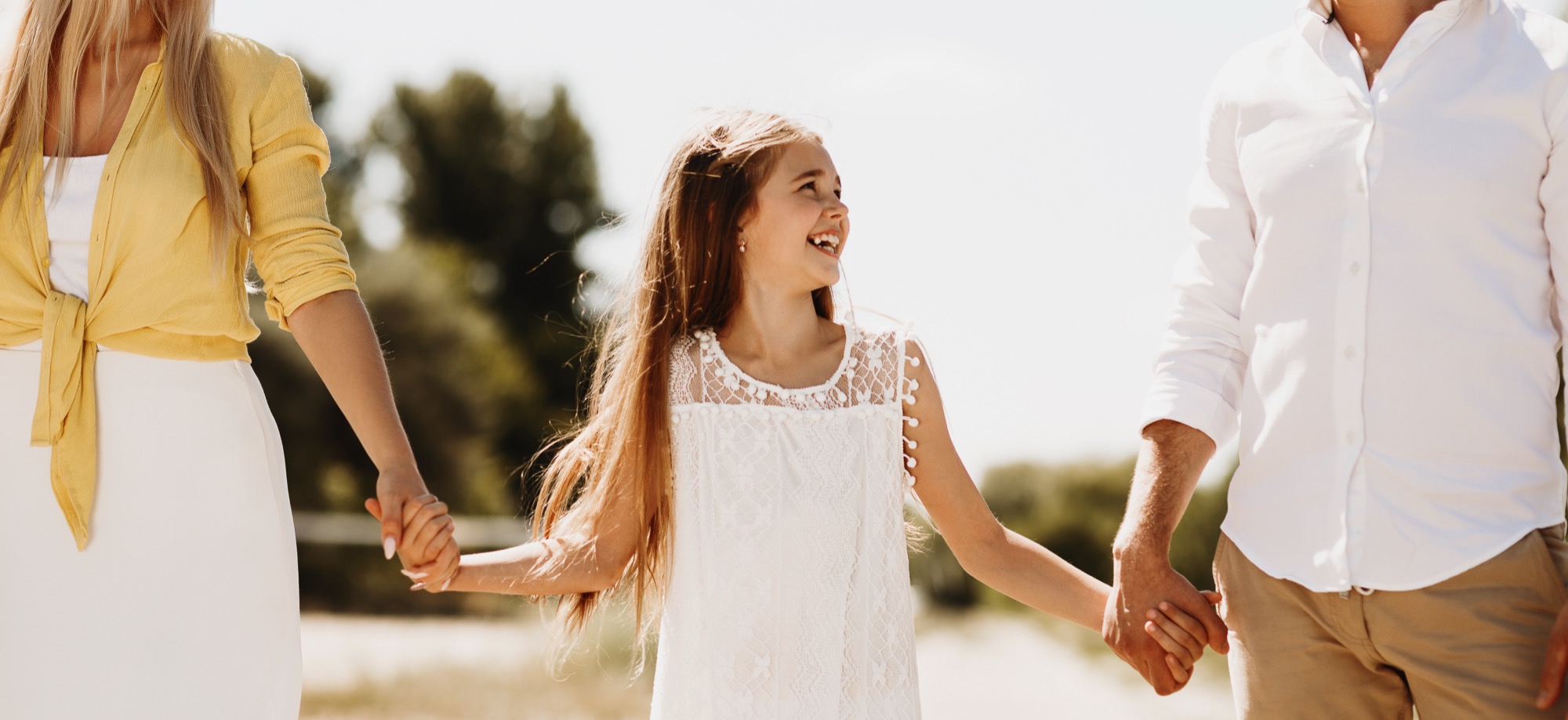 A mother, smiling daughter, and father walking outdoors holding hands