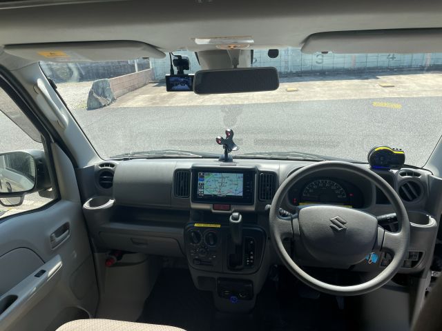Interior view of a right-hand drive Suzuki vehicle showing the steering wheel, dashboard with a GPS navigation screen, gear shift, air vents, and side mirrors.