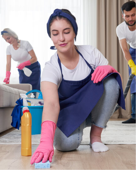 Cleaner wiping a wooden floor while teammates clean nearby.